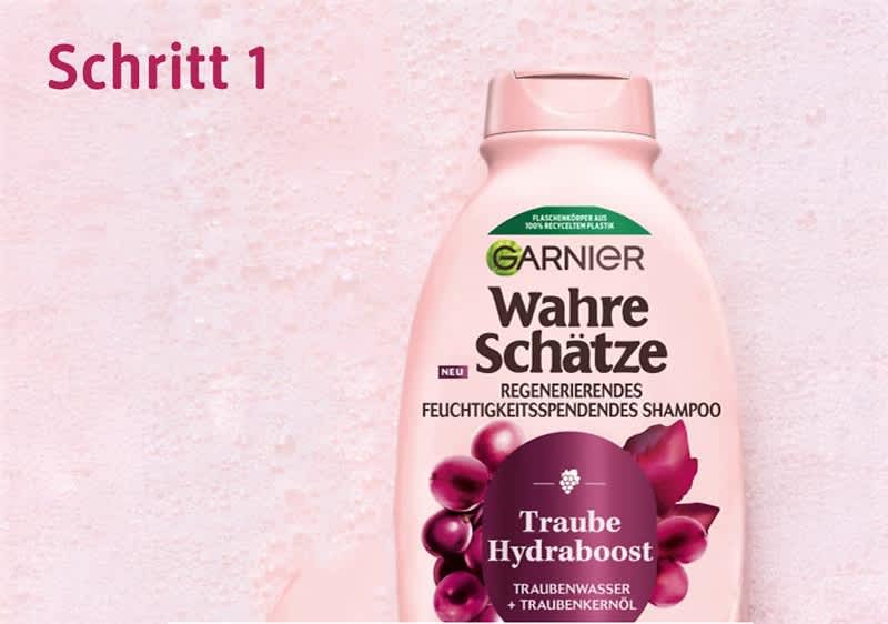 Eine rosa Shampoo-Flasche von Garnier mit der Aufschrift „Wahre Schätze Regenerierendes Feuchtigkeitsspendendes Shampoo“. Oben links steht „Schritt 1“ in roter Schrift.