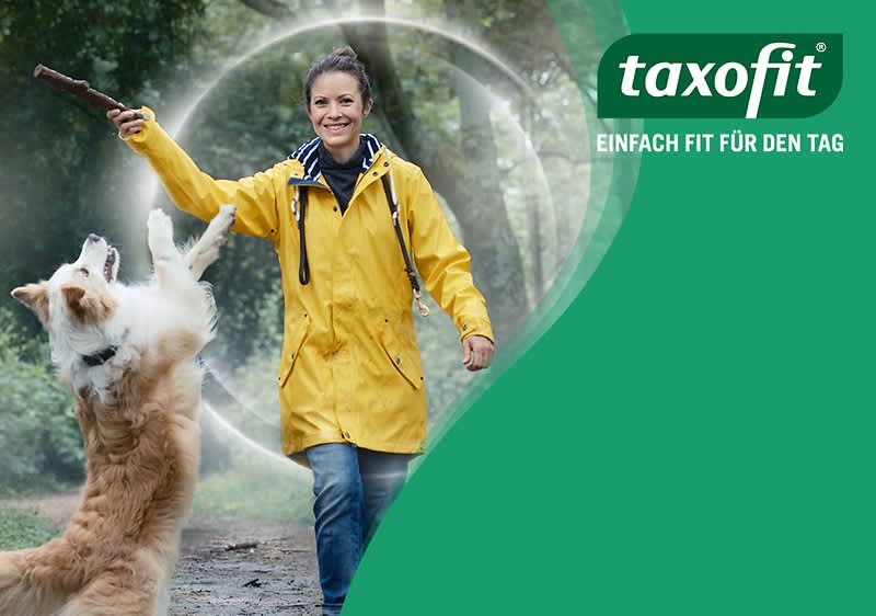 Eine Person im gelben Regenmantel spielt mit einem springenden Hund, der nach einem Stock greift. Links das Logo von Taxofit mit dem Slogan „Einfach fit für den Tag“. Fußnote: Vitamin C, Vitamin D, Zink und Selen tragen zu einer normalen Funktion des  Immunsystems bei. 