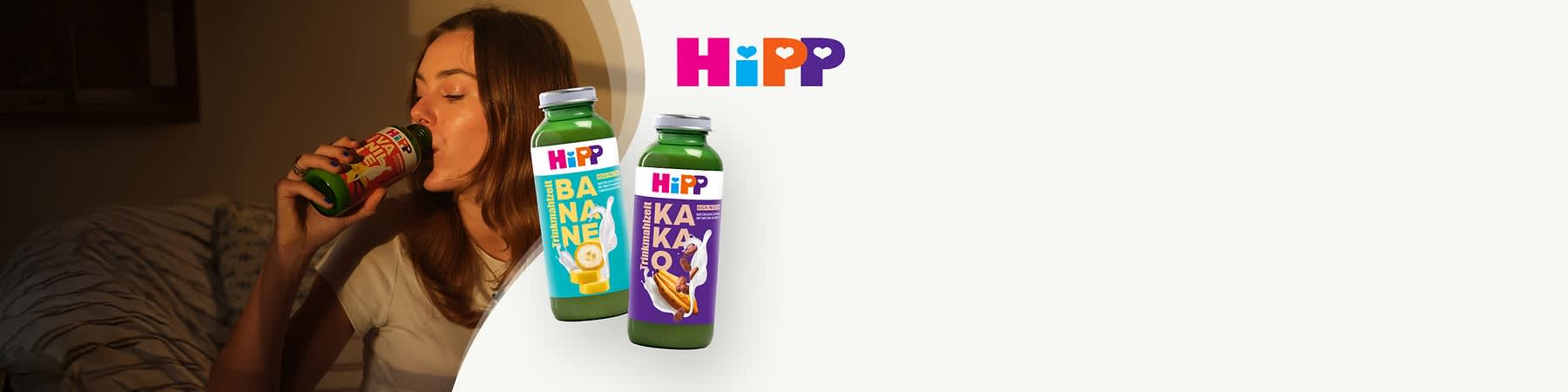 Zwei grüne Flaschen mit Etiketten der Marke HiPP. Die linke Flasche zeigt ein blaues Etikett mit der Aufschrift „BANANE“ und einem Bild von Bananenstücken. Die rechte Flasche hat ein violettes Etikett mit der Aufschrift „KAKAO“ und einem Bild von Kakaobohnen. Oben rechts das HiPP-Logo in bunten Buchstaben.