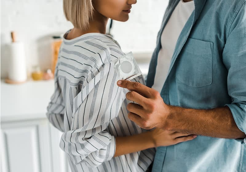 Ein Paar steht in einer Küche, der Mann hält eine Kondomverpackung in der Hand