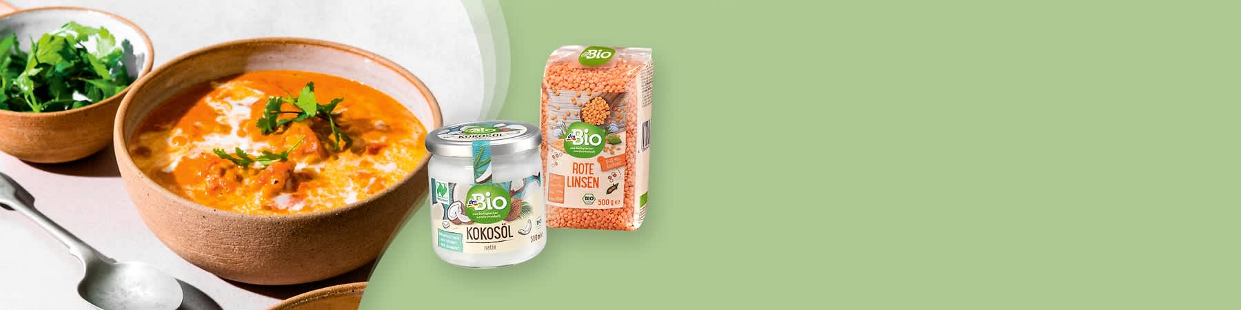 Eine Schale mit cremiger Suppe, daneben ein Glas Bio-Kokosöl und eine Packung Bio-Rote Linsen auf grünem Hintergrund