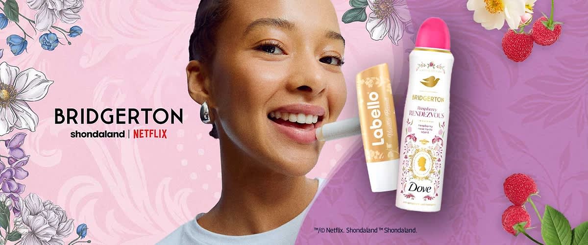 Eine Dove Deodorant-Flasche mit der Aufschrift „Bridgerton Rhapsody Rendezvous“ und ein Labello Lippenpflegestift mit der Aufschrift „Bridgerton“ liegen auf einem violetten Hintergrund mit floralen Illustrationen. Oben rechts steht „BRIDGERTON shondaland | NETFLIX“