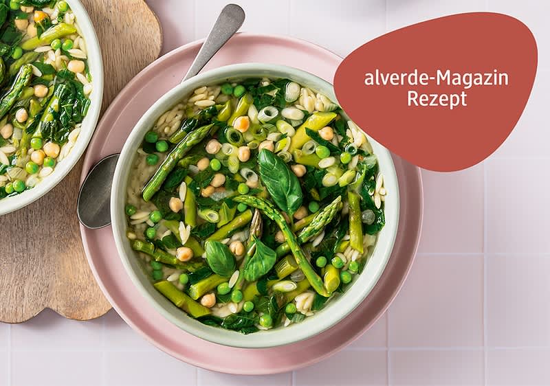 Minestrone mit Spargel, Erbsen, Kichererbsen und Blattspinat, dekoriert mit frischen Basilikumblättern, daneben ein Löffel und ein rotes feld mit dem Text „alverde-Magazin Rezept“