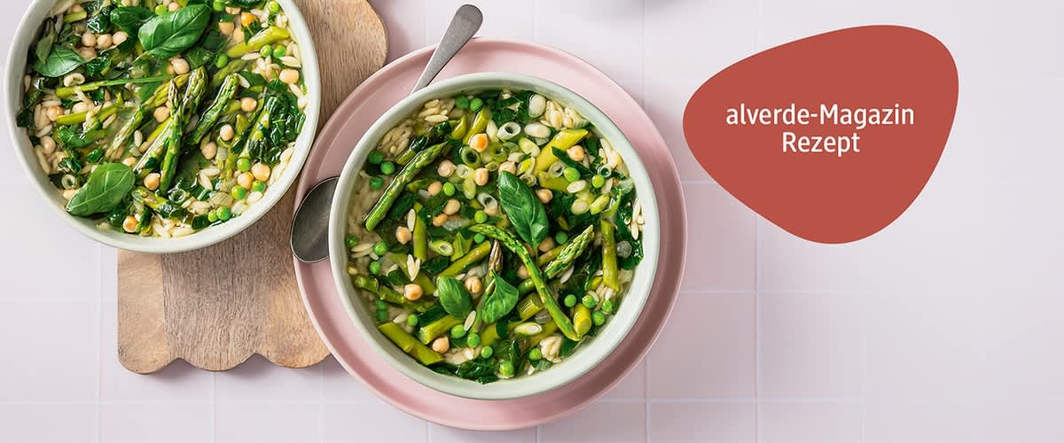 Minestrone mit Spargel, Erbsen, Kichererbsen und Blattspinat, dekoriert mit frischen Basilikumblättern, daneben ein Löffel und ein rotes feld mit dem Text „alverde-Magazin Rezept“