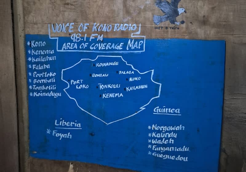 Eine handgemalte Karte auf einer blauen Tafel zeigt das Sendegebiet von Voice of Kono Radio 98.1 FM. Die Karte umfasst Orte wie Kono, Kenema, Kailahun, Falaba, Portloko, Bombali, Tonkolili und Koinadugu. Rechts sind weitere Orte in Guinea und Liberia aufgeführt.
