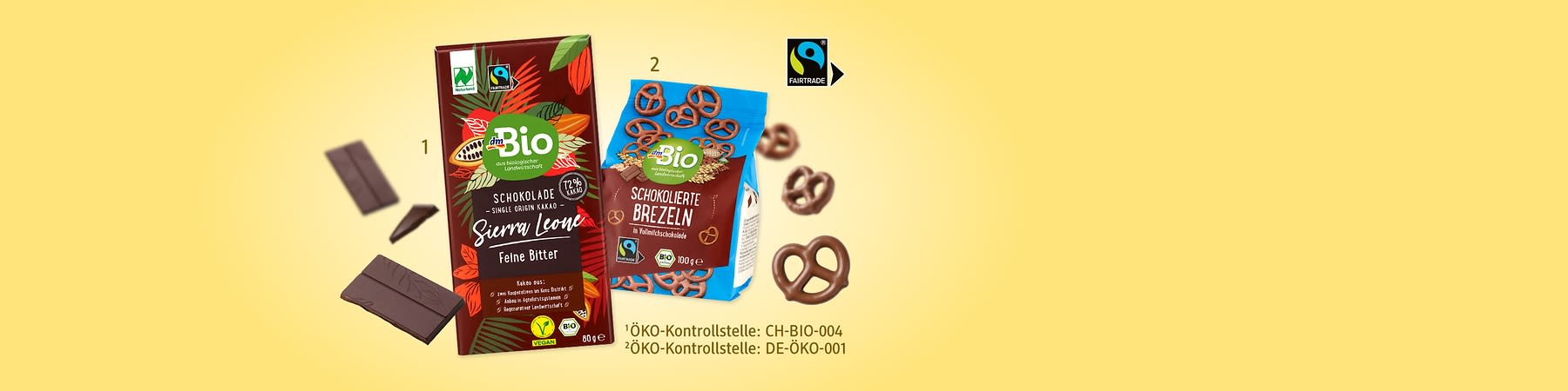 Eine braune Verpackung mit der Aufschrift „Bio Schokolade Sierra Leone Fein Bitter“ und daneben eine blaue Tüte mit der Aufschrift „Schokolierte Brezeln“ sowie mehrere Brezeln und ein Stück Schokolade davor