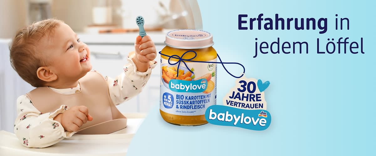 Kleinkind sitzt im Hochstuhl und hält einen Löffel, daneben Glas Babynahrung der Marke babylove mit Aufschrift „Bio Karotten mit Süßkartoffel & Rindfleisch“, dazu Schriftzug „Erfahrung in jedem Löffel“ und Emblem „30 Jahre Vertrauen babylove“