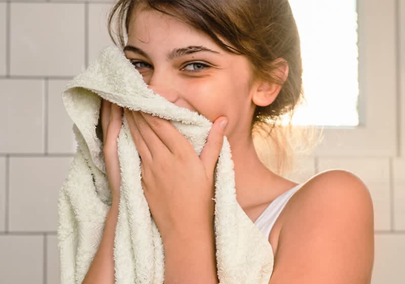Eine Person trocknet ihr Gesicht nach dem Abschminken mit einem hellen Handtuch im Badezimmer ab.