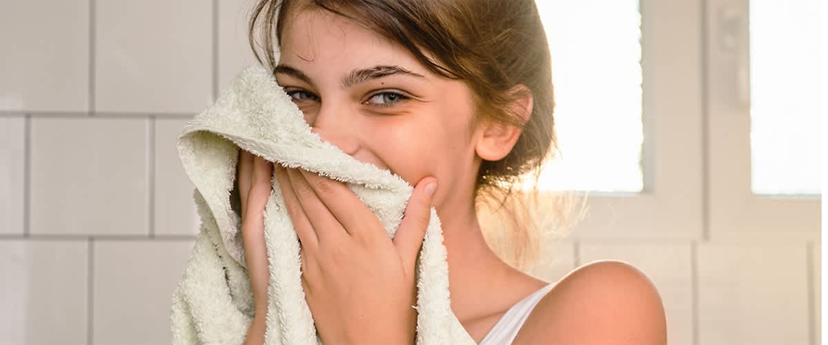 Eine Person trocknet ihr Gesicht nach dem Abschminken mit einem hellen Handtuch im Badezimmer ab.