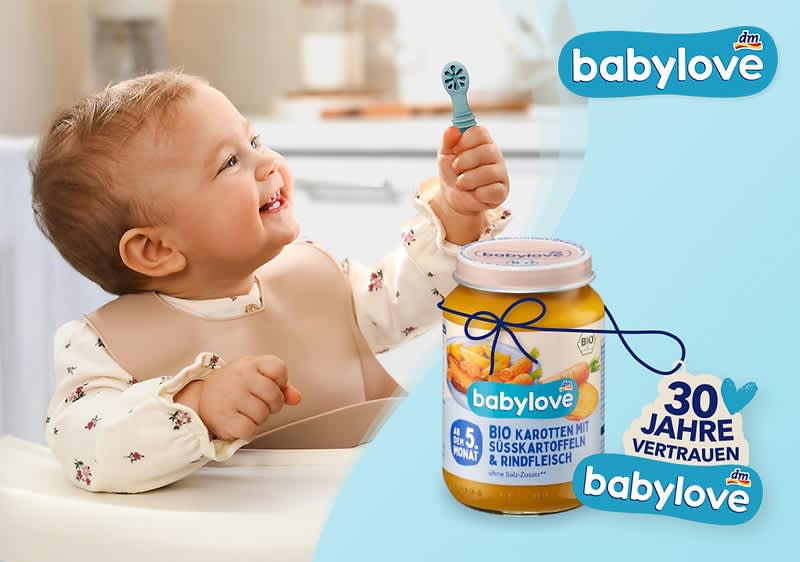 Ein Baby hält einen Löffel in der Hand. Daneben ein Glas Babylove Bio-Karotten mit Süßkartoffeln und Rindfleisch. Rechts oben das Babylove-Logo und ein Herz mit der Aufschrift „30 Jahre Vertrauen“.