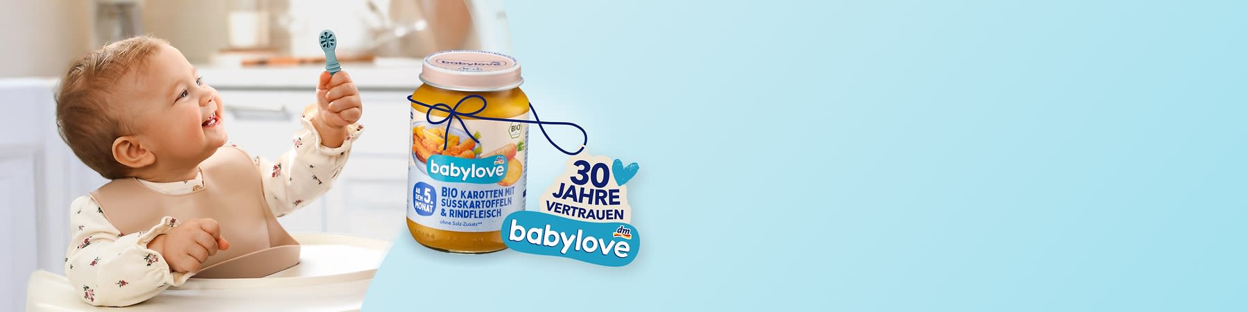 Kleinkind im Hochstuhl greift mit einem Löffel nach einem Babynahrungsglas „babylove“; neben dem Glas Textaufdruck „30 Jahre Vertrauen“ und Etikett „Babylove Bio Karotten mit Süßkartoffeln & Rindfleisch“