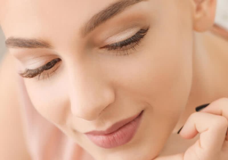 Eine Person hält einen Wimpernzange in der Hand und trägt ein Augen Make-up in dem die Wimpern im Vordergrund stehen