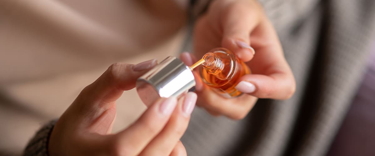 Eine Person hält eine kleine Glasflasche mit Nagelöl in der Hand
