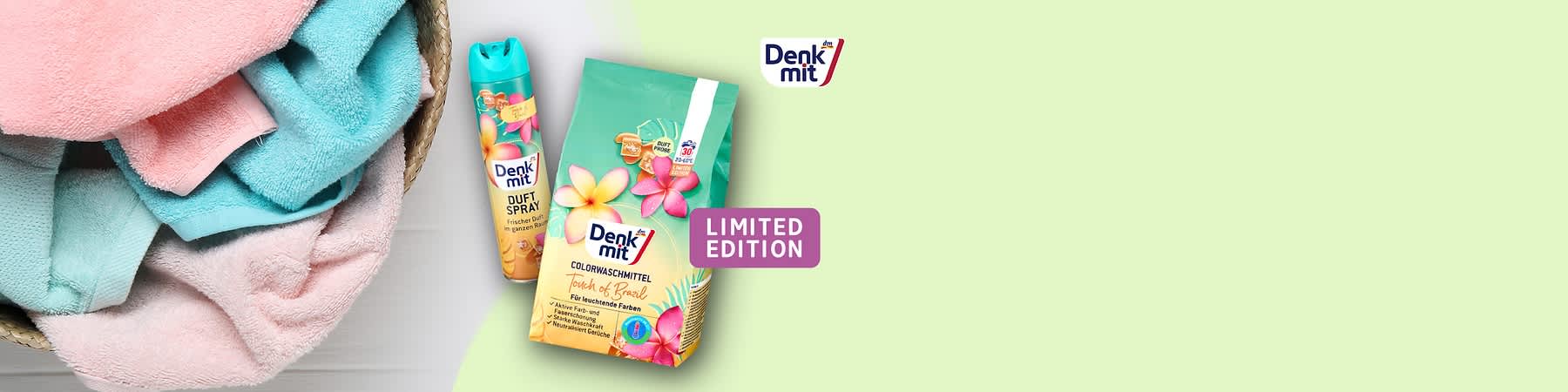 Eine Packung Denkmit Colorwaschmittel Tropical & Brazil mit bunten Blumen und eine Dose Denkmit Duftspray Frischer Duft sind neben gefalteten Handtüchern abgebildet. Oben rechts ist das Denkmit-Logo zu sehen