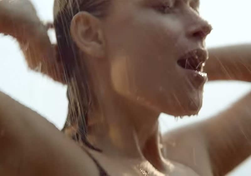 Eine Person steht unter einem Wasserstrahl und hält ihre Haare mit beiden Händen zurück