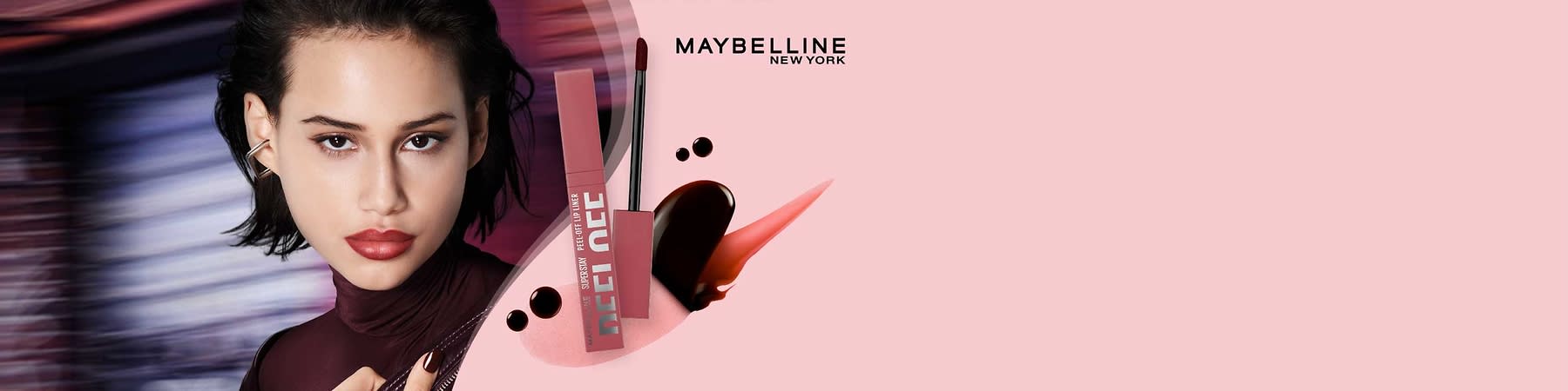 rosa-violette Maybelline Superstay Peel Off Lip-Gloss-Verpackung mit aufgesetztem Applikator und Lippenfarbspuren vor rosa Hintergrund, oben rechts Schriftzug „MAYBELLINE NEW YORK“