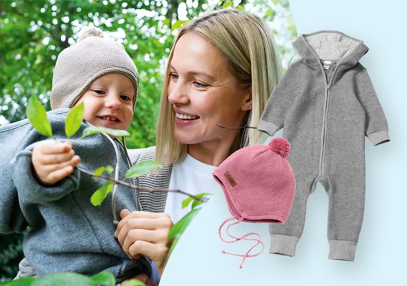 Ein grauer Baby-Overall mit Kapuze und ein rosa Mützchen mit Bommel auf hellblauem Hintergrund. Links daneben hält eine Person ein Kleinkind, beide tragen ähnliche Kleidung.