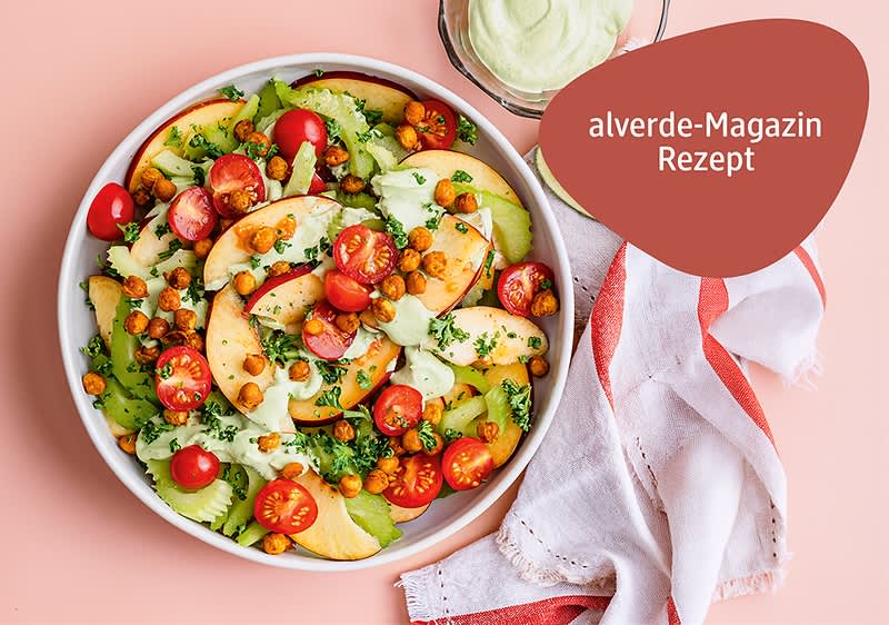 Schüssel mit Salat aus Pfirsichscheiben, halbierten Kirschtomaten, Selleriescheiben, gebackenen Kichererbsen und grüner Kräutercreme, daneben ein Glas mit Dressing und ein weiß-rotes Tuch, oben rechts roter Badge mit Text „alverde-Magazin Rezept“