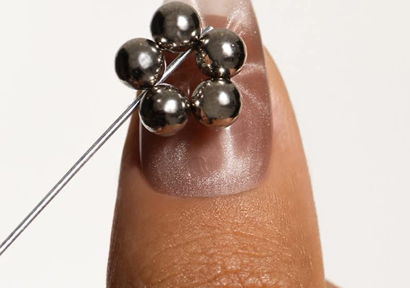 Eine Hand hält eine Nadel, die durch fünf silberne Perlen geführt ist, die auf einem Finger ruhen.