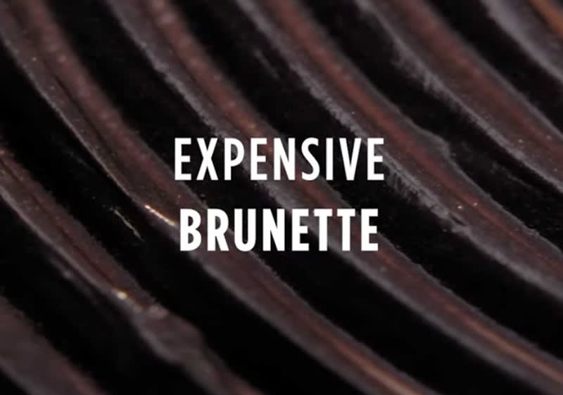 Dunkle, glänzende Oberfläche mit dem weißen Text „Expensive Brunette“