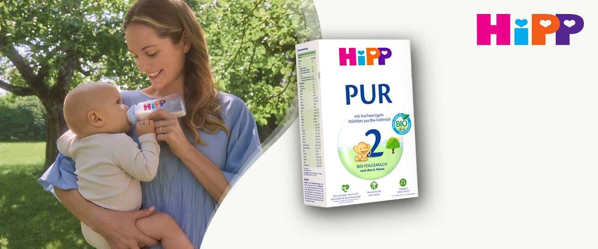 Frau im blauen Kleid hält ein Baby im Arm und füttert es mit einer Babyflasche, oben rechts Logo „HiPP“