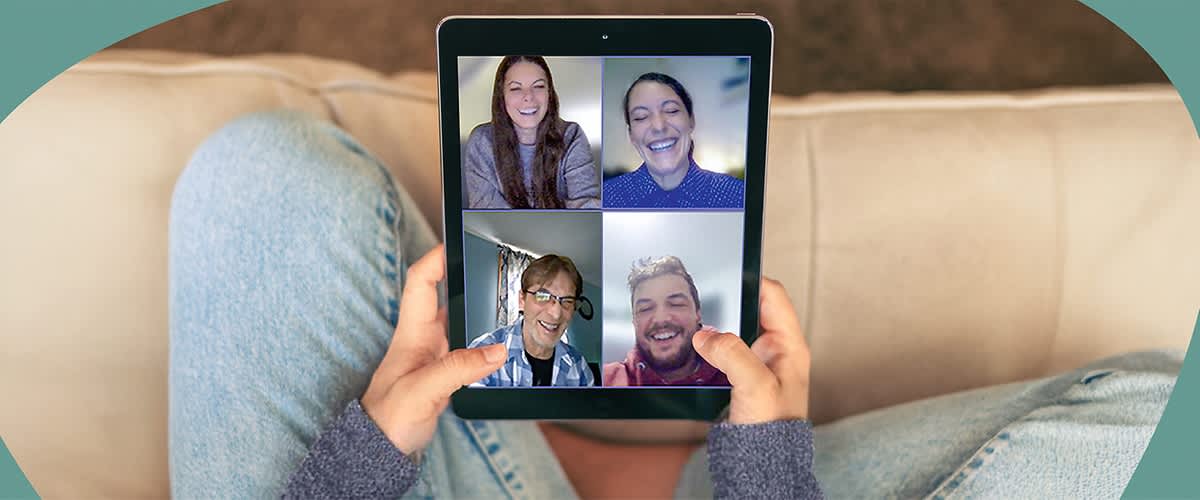 Eine Person hÀlt ein Tablet, auf dem ein Videoanruf mit vier Teilnehmern angezeigt wird.