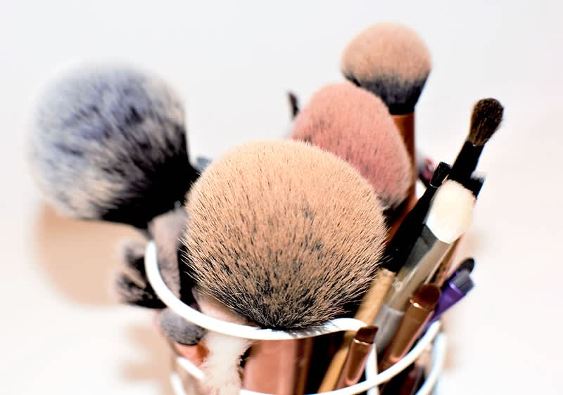 Mehrere Make-up-Pinsel in einem weißen Behälter, darunter große Puderpinsel und kleinere Lidschattenpinsel