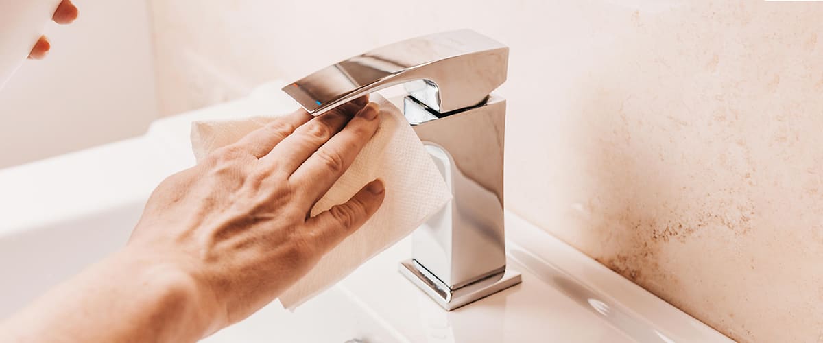 Eine Hand wischt mit einem weißen Tuch einen glänzenden Wasserhahn ab