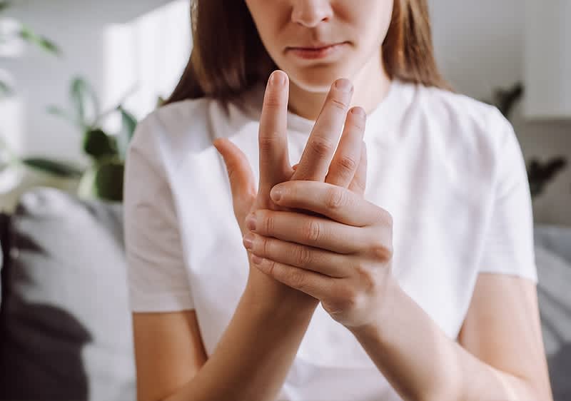 Eine Person in einem weißen T-Shirt hält ihre Hand und scheint Schmerzen zu haben