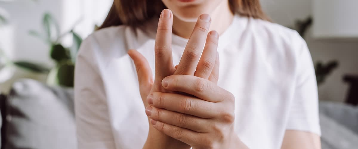 Eine Person in einem weißen T-Shirt hält ihre Hand und scheint Schmerzen zu haben