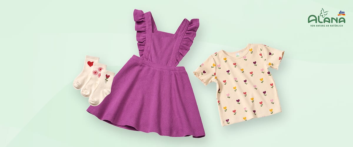 Ein lila Kinderkleid mit Rüschenärmeln, daneben ein cremefarbenes T-Shirt mit bunten Blumenmotiven und drei Paar weiße Socken mit Herz- und Blumenmustern. Oben rechts das Logo von Alana und dm.