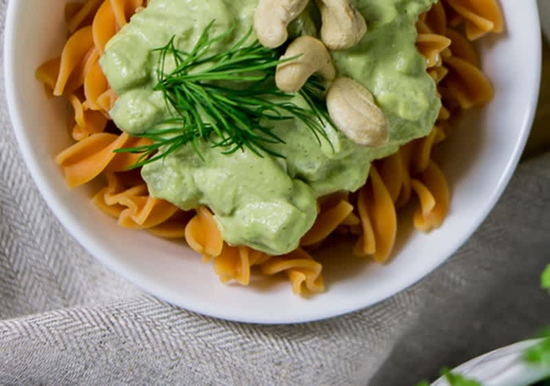 Ein Teller mit rotbraunen Fusilli-Nudeln, darauf eine grüne Kohlrabi-Creme, garniert mit frischem Dill und Cashewnüssen