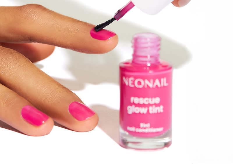 Eine Hand mit pink lackierten Nägeln hält einen Nagellackpinsel über einem geöffneten Fläschchen mit der Aufschrift „NEONAIL rescue glow tint“
