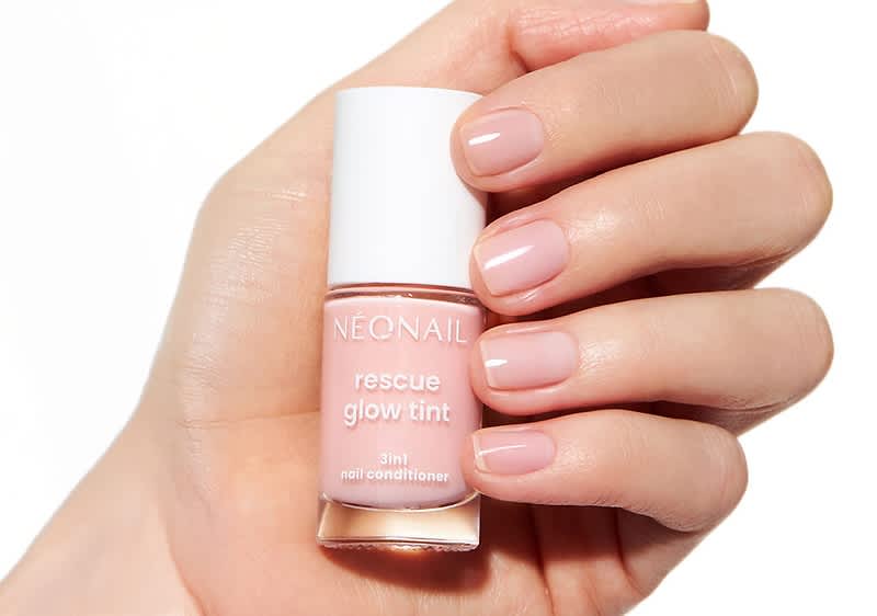 Eine Hand mit gepflegten, hellrosa lackierten Nägeln hält eine Flasche Nagellack von NEONAIL mit der Aufschrift „rescue glow tint 3in1 nail conditioner“