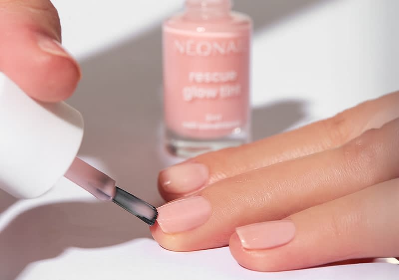 Eine Hand wird mit einem hellrosa Nagellack von Neonal lackiert, im Hintergrund steht die Flasche mit der Aufschrift „rescue glow tint“