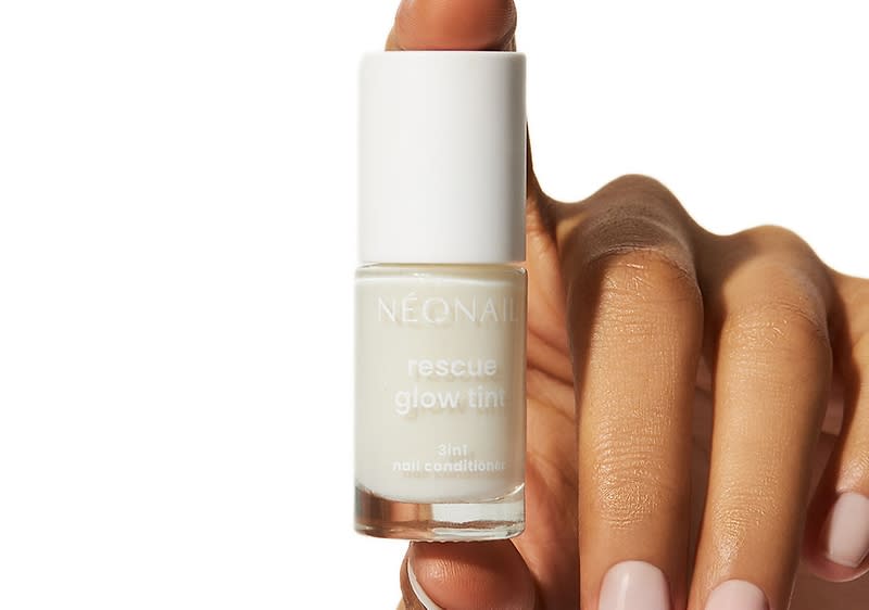 Eine Hand hält eine Flasche mit weißem Deckel und der Aufschrift „NÉONAIL rescue glow tint 3in1 nail conditioner“