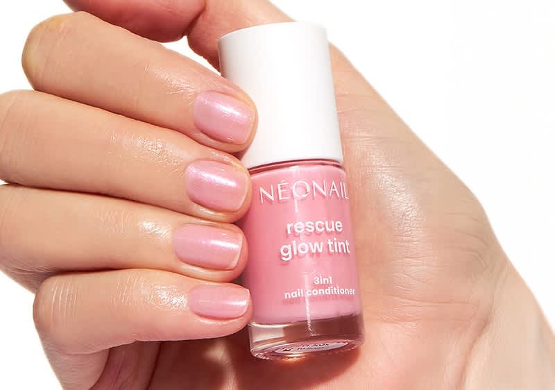Eine Hand hält eine Flasche mit rosa Nagelpflege von NÉONAIL mit der Aufschrift „rescue glow tint 3in1 nail conditioner“
