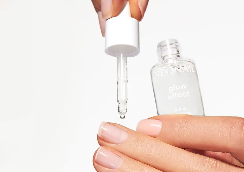 Eine Hand hält eine Pipette über eine Flasche mit der Aufschrift „NEONAIL glow effect quick“, während eine andere Hand mit gepflegten Nägeln darunter positioniert ist.