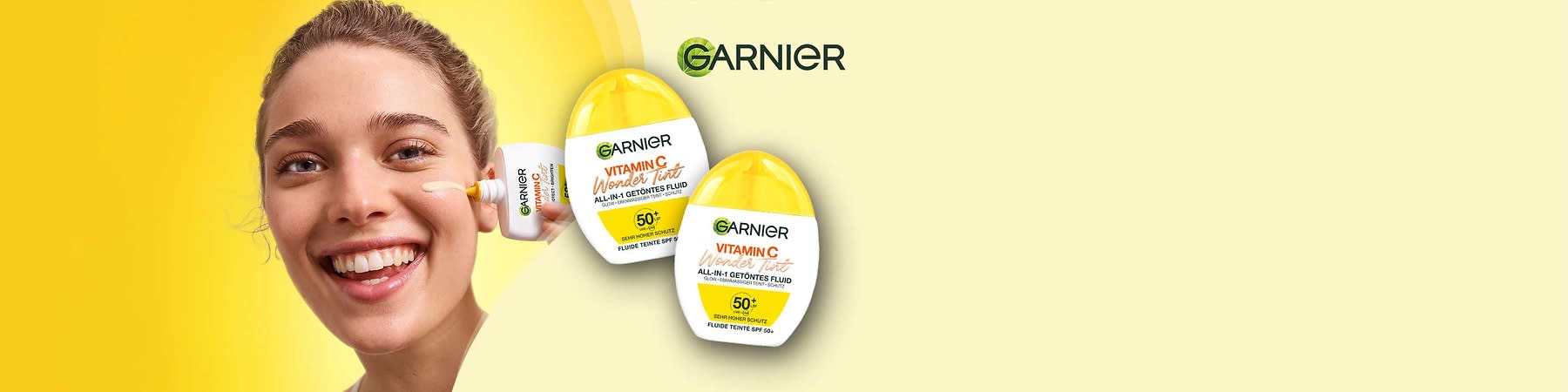 Zwei gelbe Flaschen des Garnier Vitamin C Wonder Tint Fluids mit der Aufschrift „ALL-IN-1 GETÖNTES FLUID“ und „SEMI-MATTE SCHUTZ FLUIDE TEINTE SPF 50+“. Oben rechts das Logo von Garnier