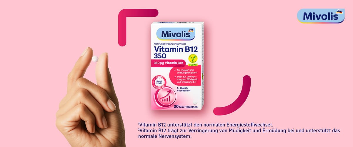 Hand, die eine kleine weiße Tablette zwischen Daumen und Zeigefinger hält, daneben eine weiße Verpackung des Nahrungsergänzungsmittels „Mivolis Vitamin B12 350“ mit blauem Logo, rosa Akzenten, dem Hinweis „350 µg Vitamin B12“, einem Vegan-Symbol und der Angabe „30 Mini-Tabletten“, vor hellrosa Hintergrund