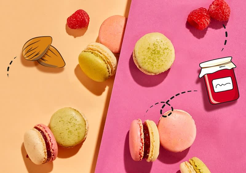 Macarons in verschiedenen Farben liegen auf einem orangefarbenen und einem pinken Hintergrund, begleitet von Himbeeren, einer gezeichneten Mandel und einem gezeichneten Marmeladenglas.