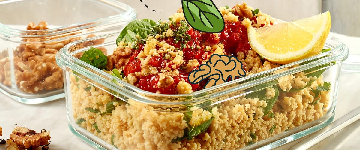 Ein Glasbehälter mit Couscous, garniert mit Tomatensauce, frischen Kräutern und einer Zitronenscheibe. Daneben eine Schale mit Walnüssen und ein Glas Wasser. Illustrationen von einem Herz und einem Basilikumblatt sind über dem Couscous platziert.