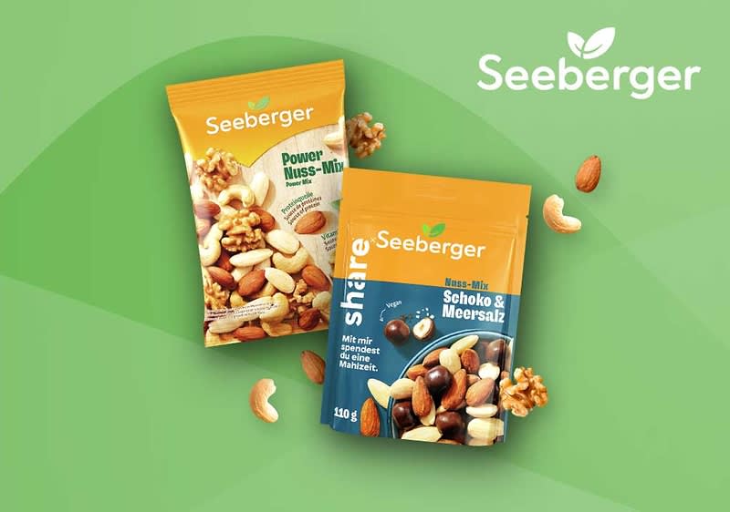 Zwei Seeberger Snack-Packungen auf grünem Hintergrund: links eine orange-gelbe Tüte mit der Aufschrift „Seeberger Power Nuss-Mix“ und Abbildung verschiedener Nüsse, rechts eine orange-blaue Tüte mit der Aufschrift „Seeberger share Schoko & Meersalz“ mit Abbildung von Nüssen und Schokoladenstücken, umgeben von einzelnen Mandeln, Cashewkernen und Walnussstücken, ober rechts das Seeberger-Logo ohne Punkt am Ende