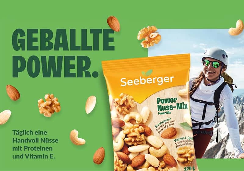 Grüne Werbefläche mit der überschrift „GEBALLTE POWER“, links unten Text „Täglich eine Handvoll Nüsse mit Proteinen und Vitamin E“, in der Bildmitte eine orange-gelbe Seeberger-Packung „Power Nuss-Mix“ mit sichtbaren Cashews, Mandeln und Walnussstücken, rechts ein abgetrenntes Foto einer in Bergsportkleidung stehenden Person mit Helm vor verschneiten Bergen, mehrere einzelne Nüsse verteilt über das Motiv