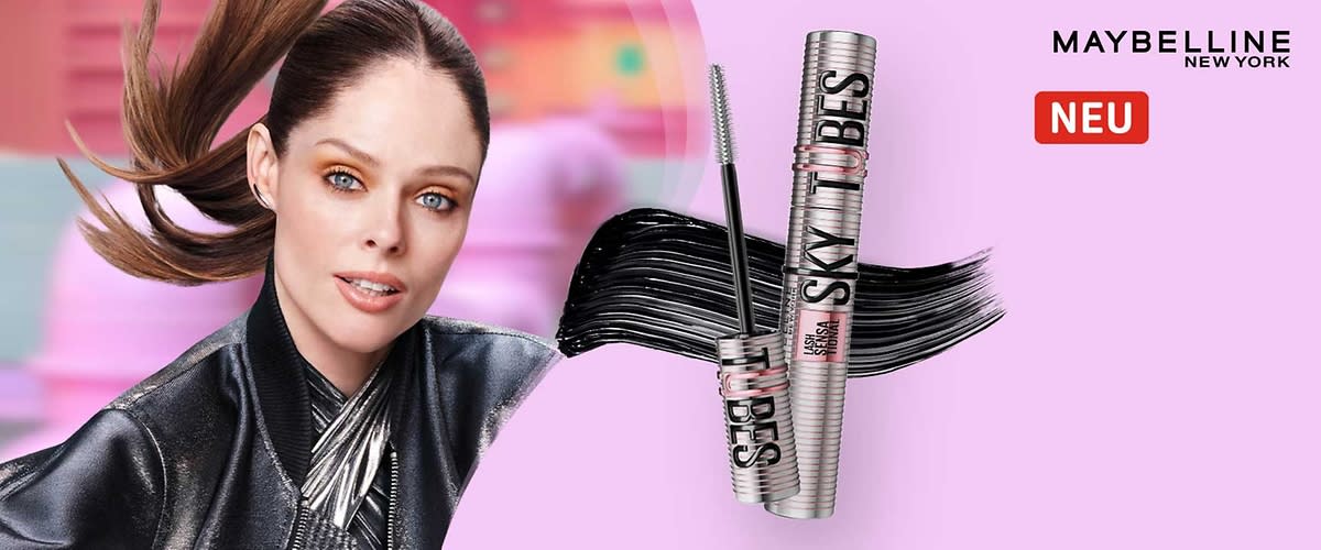 Zwei silberne Maybelline Sky High Mascara-Röhrchen, eines geöffnet mit sichtbarer Bürste, vor schwarzem Mascara-Strich auf hellrosa Hintergrund; oben rechts das Maybelline New York-Logo und daneben rotes Feld mit der Aufschrift „NEU“