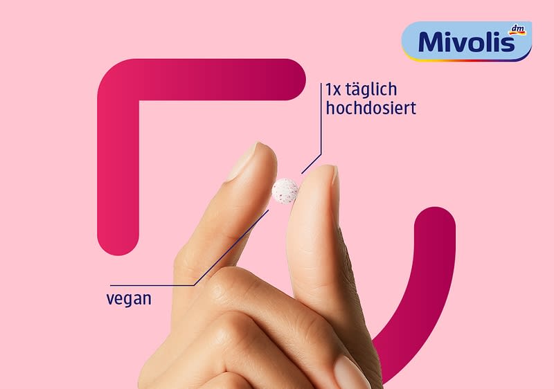 Hand hält zwischen Daumen und Zeigefinger eine kleine weiße Tablette mit sichtbaren Punkten, daneben Text „1x täglich hochdosiert“ und „vegan“, oben rechts das Logo von Mivolis auf rosa Hintergrund