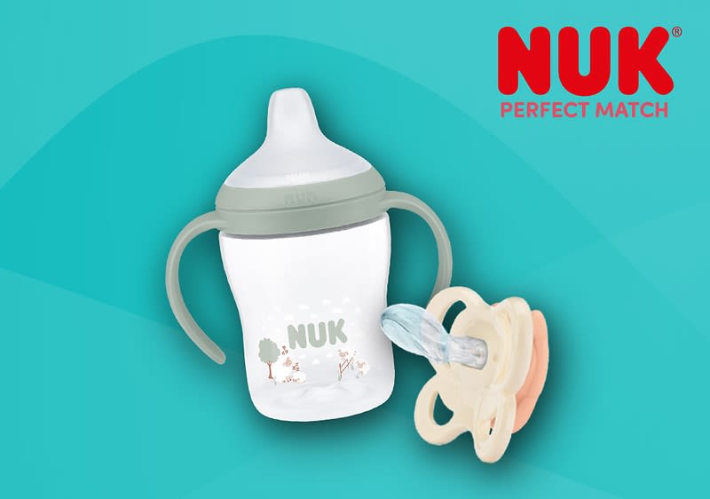 Eine NUK-Trainingsflasche mit zwei seitlichen Griffen und hellem Sauger, weißer Flasche mit kleinem Waldmotiv und dem Schriftzug „NUK“, daneben ein beige-rosa Schnuller mit transparentem Sauger, rotes NUK-Logo oben rechts