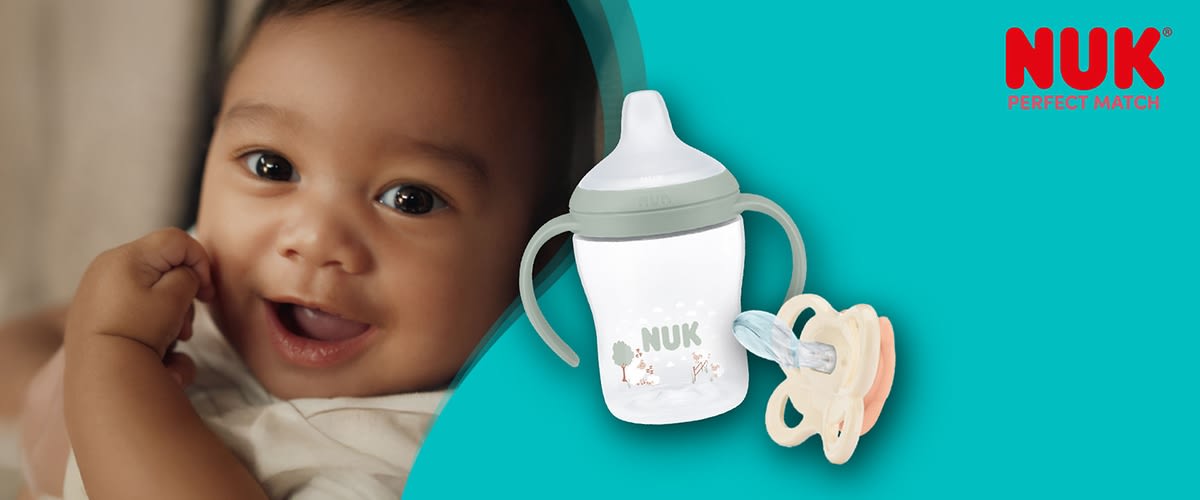 Eine NUK-Trainingsflasche mit zwei seitlichen Griffen und hellem Sauger, weißer Flasche mit kleinem Waldmotiv und dem Schriftzug „NUK“, daneben ein beige-rosa Schnuller mit transparentem Sauger, rotes NUK-Logo oben rechts