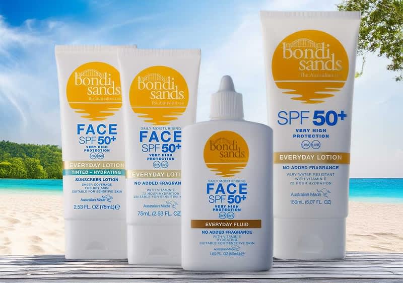 Vier weiße Sonnenschutzprodukte der Marke Bondi Sands mit gelbem Logo auf sandigem Untergrund, vorn eine kleine weiße Flasche mit Tropfverschluss und Aufschrift „Face SPF 50+ Everyday Fluid No Added Fragrance“, links und rechts zwei Tuben mit Aufschrift „Face SPF 50+ Everyday Lotion“ und hinten eine größere Tube mit „Bondi Sands“ Logo sichtbar