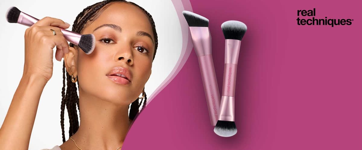 Zwei rosa Make-up-Pinsel der Marke Real Techniques mit schwarzen und weißen Borsten liegen überkreuzt auf rosa Hintergrund, rechts oben das schwarze Logo „real techniques“